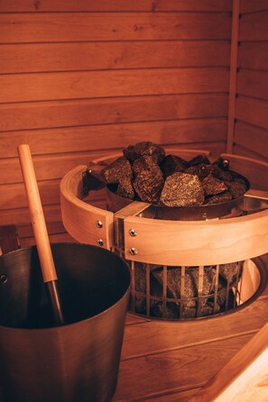 A sauna with a wooden bench and a metal container holding rocks.