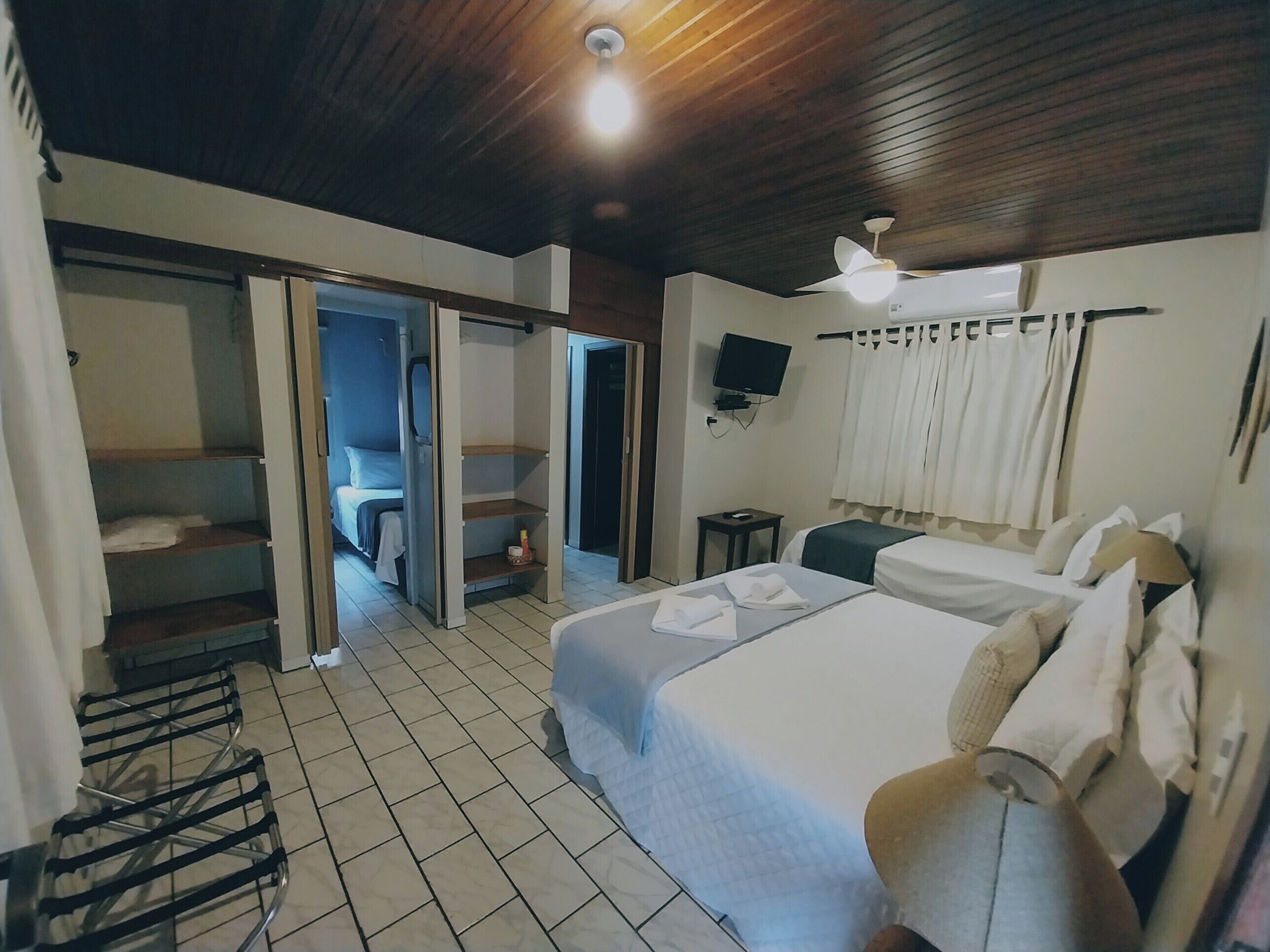 A hotel room with a bed, a TV, a ceiling fan, and a bathroom visible through an open door.