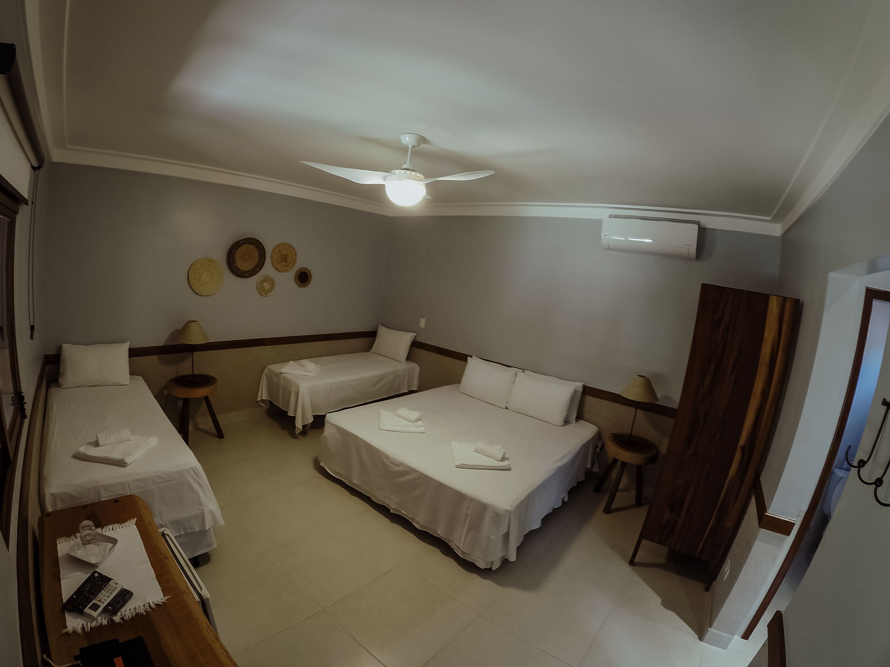 A hotel room with two single beds, a desk, a chair, a ceiling fan, and a wall-mounted air conditioner.