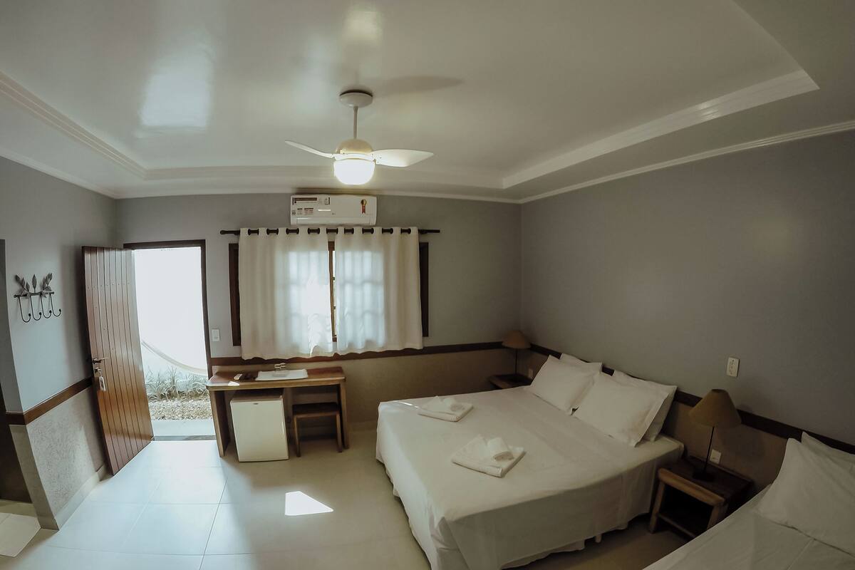A hotel room with a bed, bedside table, desk, chair, and a ceiling fan.
