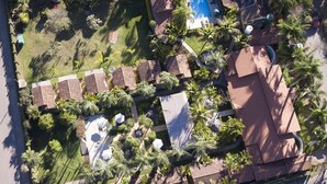 Eine Vogelperspektive zeigt ein Resort mit mehreren Bungalows, einem Schwimmbad und üppiger Bepflanzung.