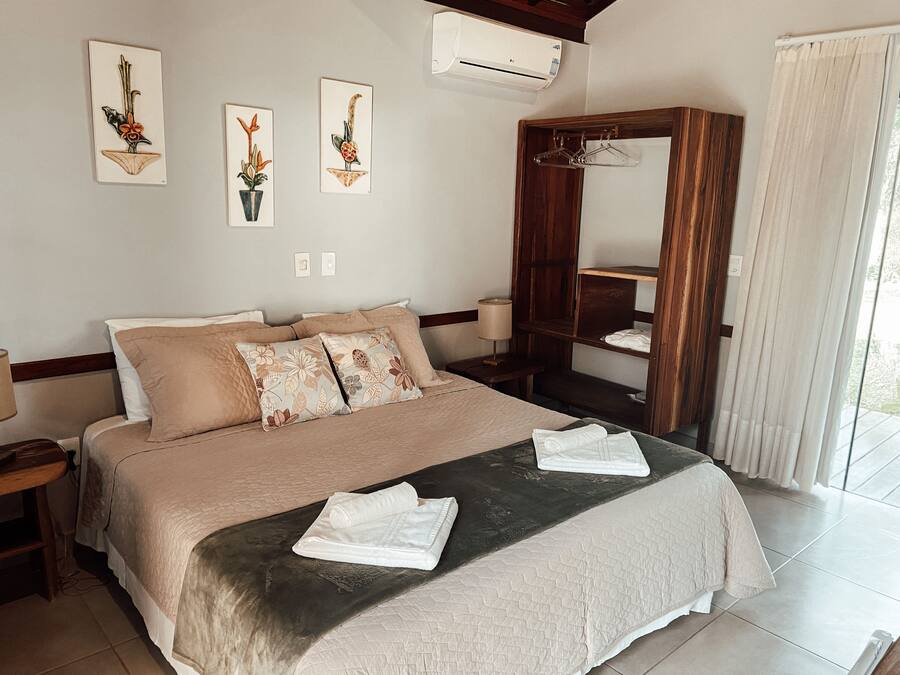 A hotel room with a large bed, a wooden wardrobe, and three wall-mounted artworks.