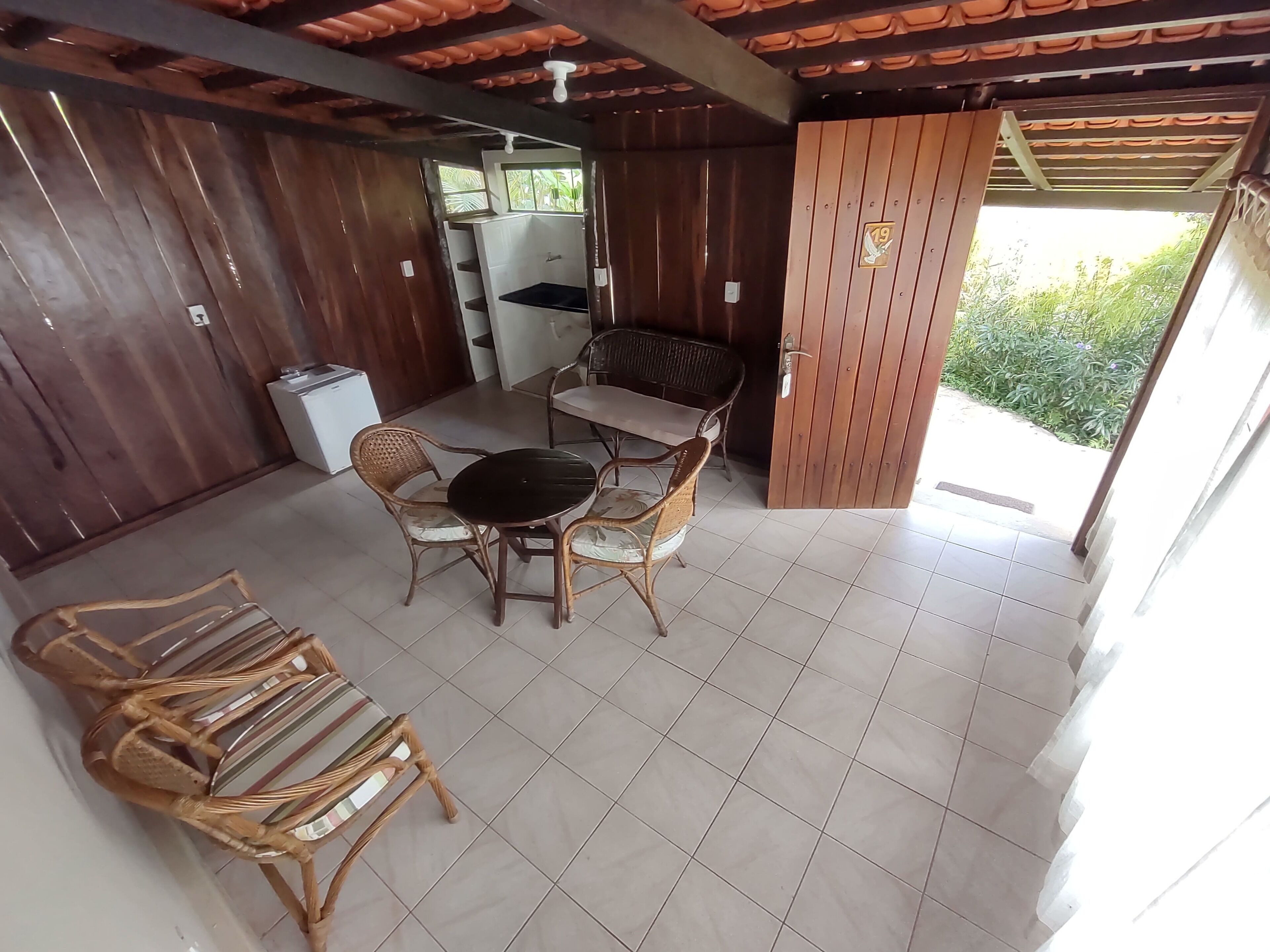 A covered outdoor area with a wooden table and chairs, a small sink, and a door leading outside.