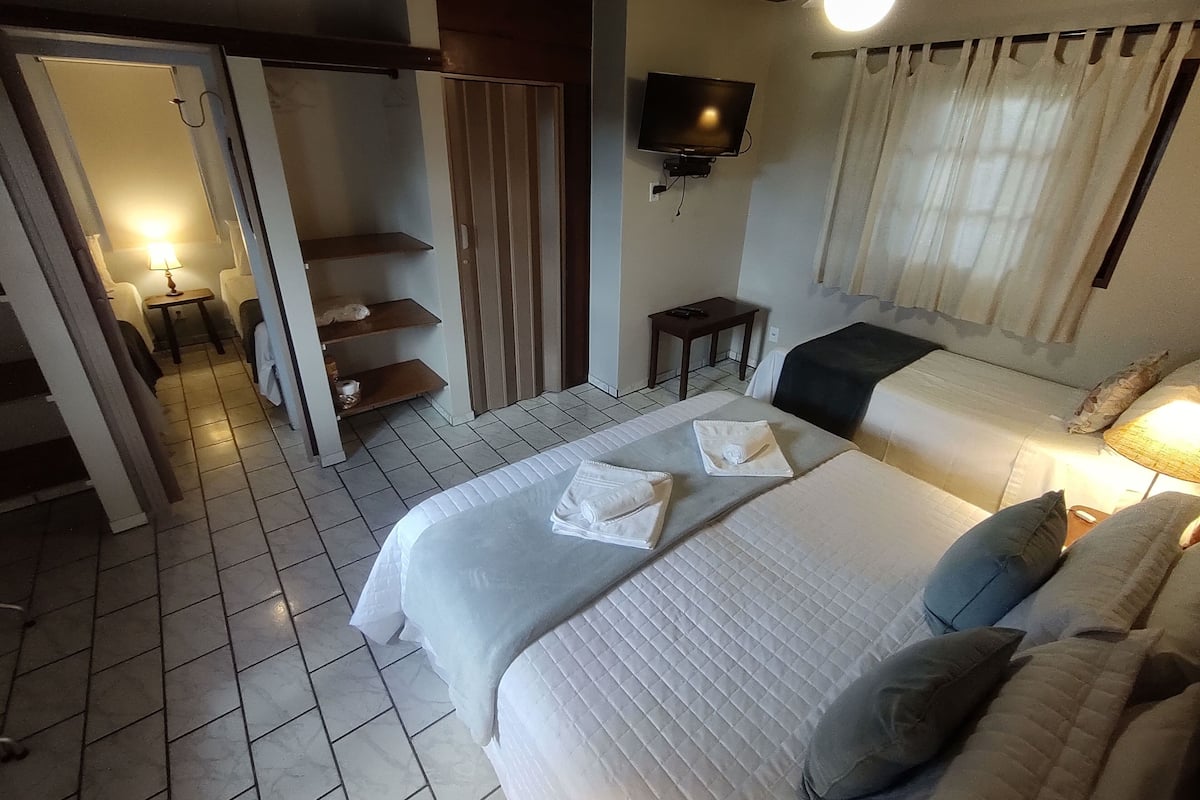 A hotel room with a bed, a TV, a small table, and a bathroom with a shower.
