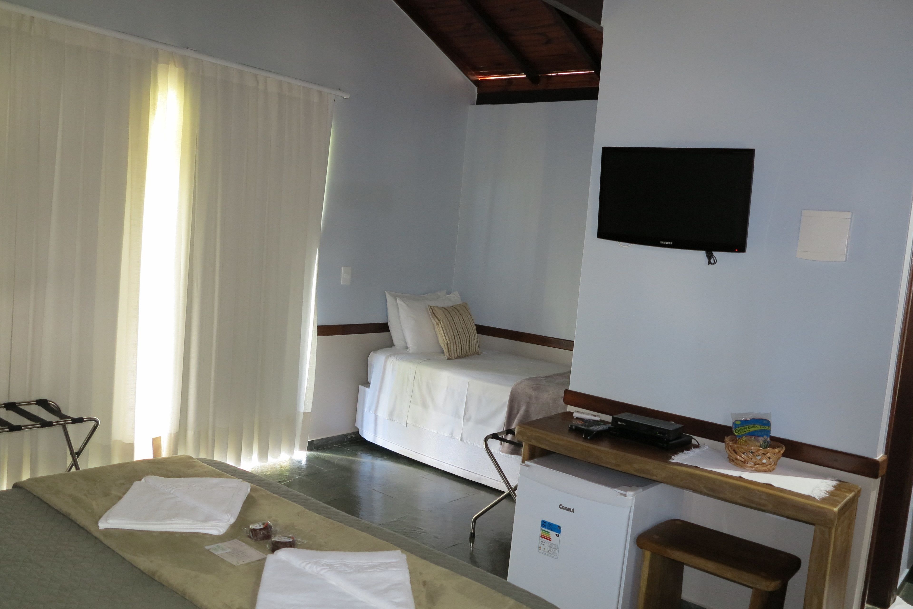 A hotel room with a bed, a desk with a computer, a television, and a small refrigerator.