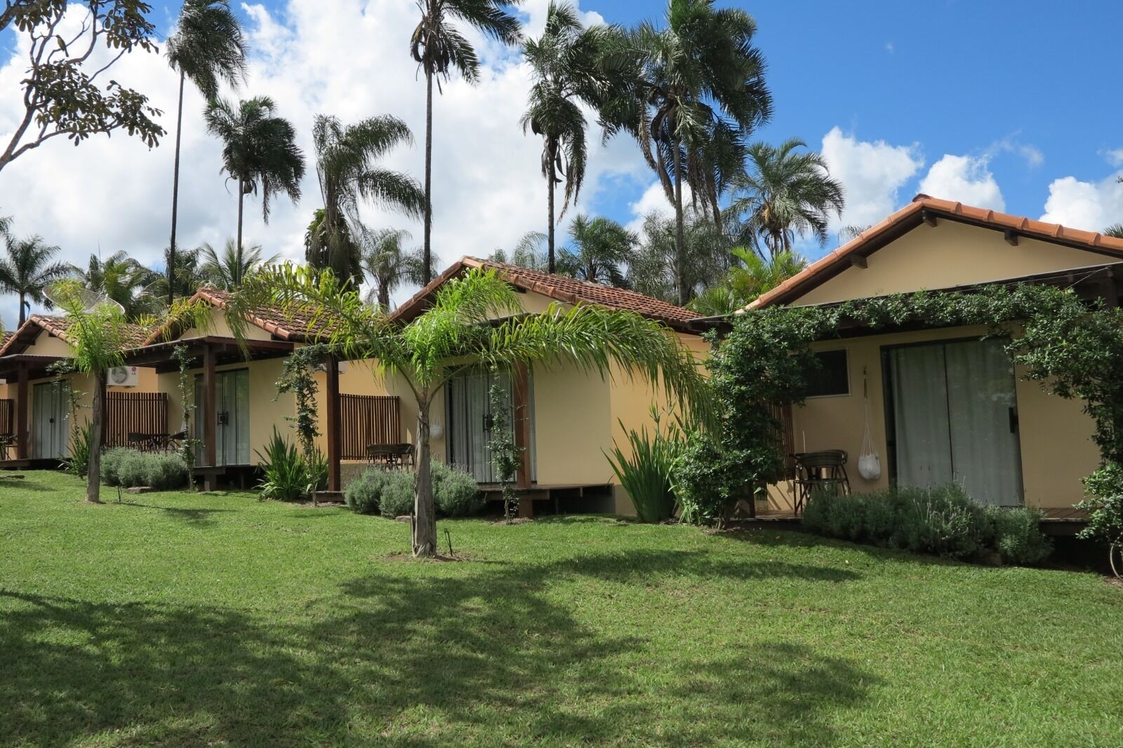 A row of single-story buildings with a tiled roof, surrounded by well-maintained grass and palm trees.