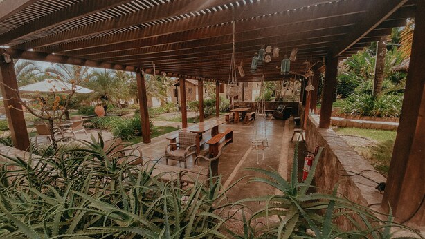 Eine Außenpatio-Terrasse mit Holztischen und -stühlen, umgeben von üppiger Bepflanzung und einer Pergola.