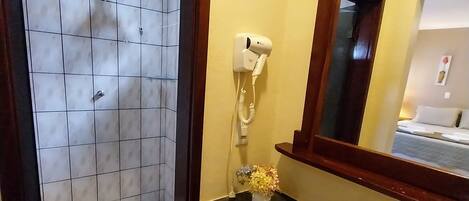 A bathroom with a shower, a sink, a hairdryer, and a mirror.