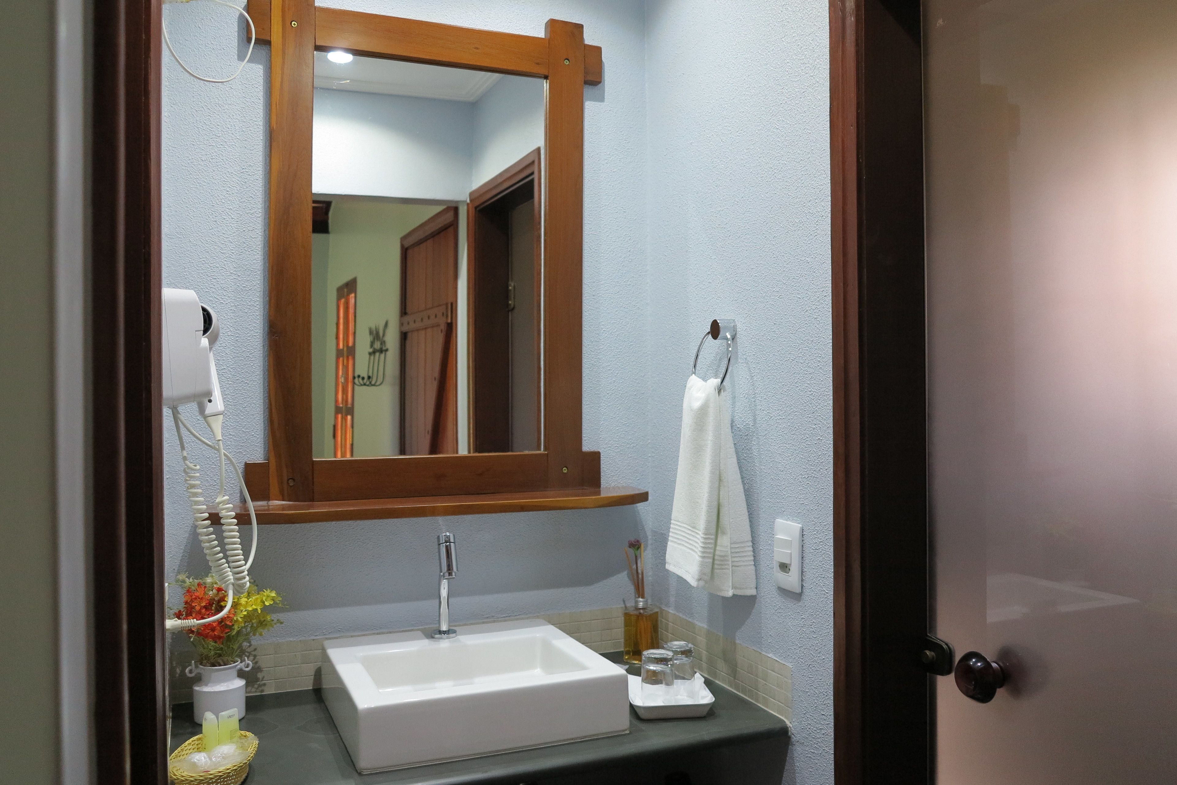 Uma casa de banho com uma pia branca, um espelho, um porta-toalhas e uma porta.
