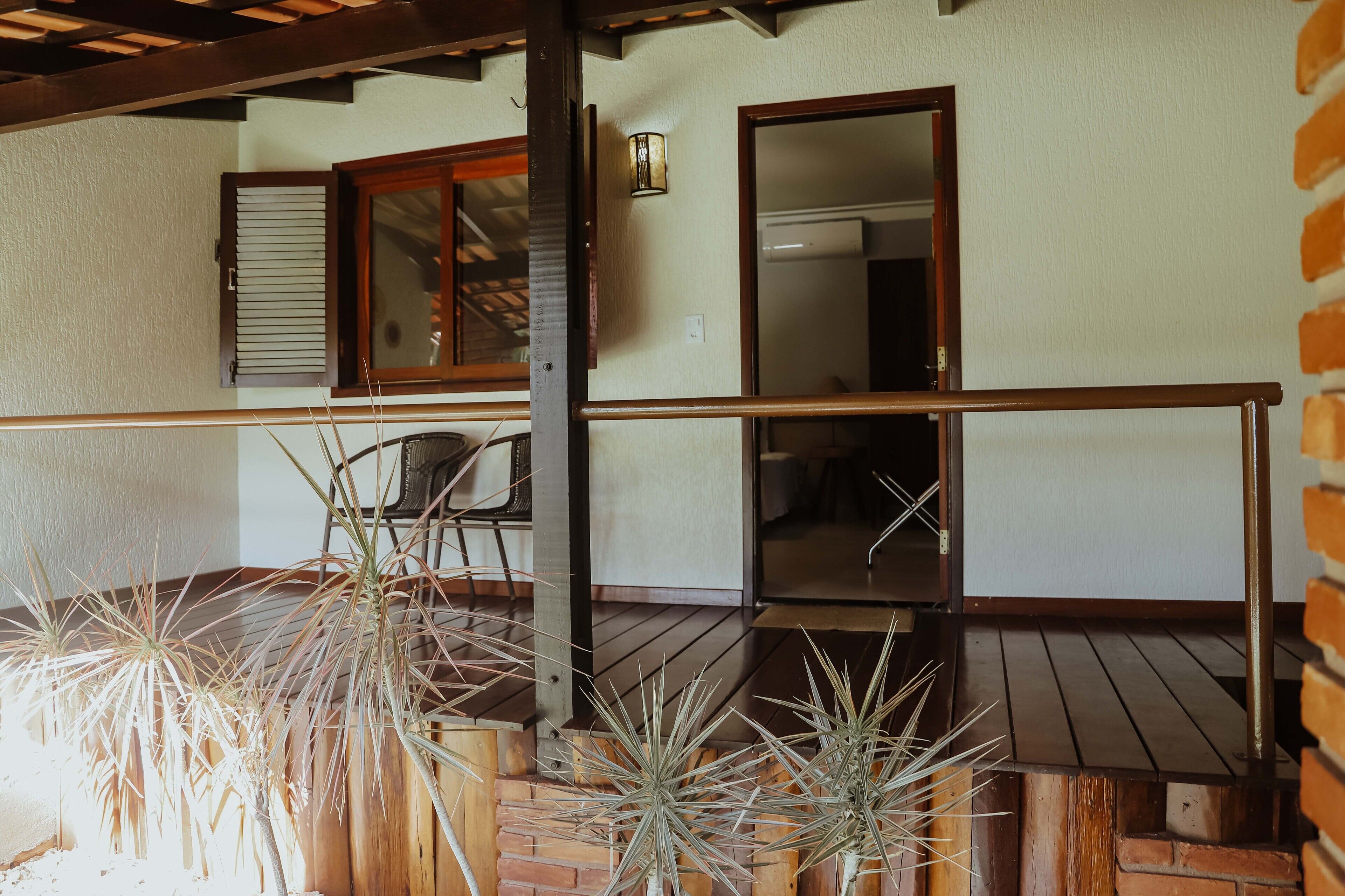 A wooden deck with potted plants, a chair, and a door leading to an interior space.