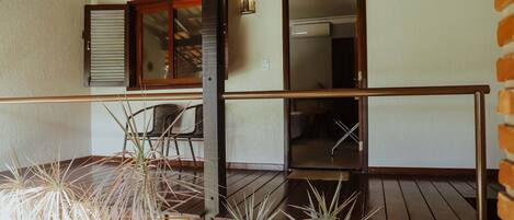 A wooden deck with potted plants, a chair, and a door leading to an interior space.