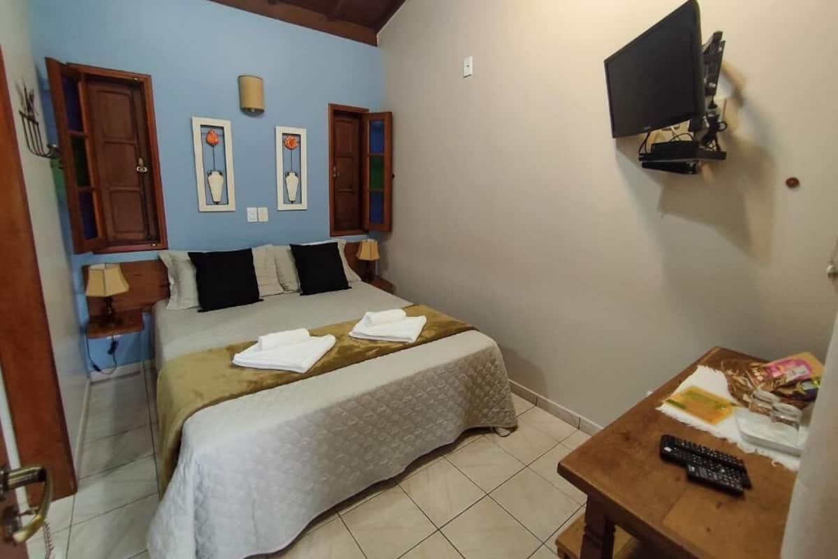 A bedroom with a bed, a TV mounted on the wall, a wooden table with a remote, and a door with a handle.