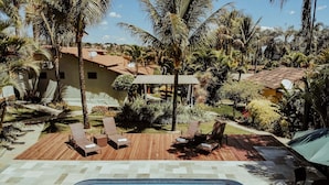 Ein Swimmingpool mit Liegestühlen und einer Holzterrasse, umgeben von Palmen und einem Garten.