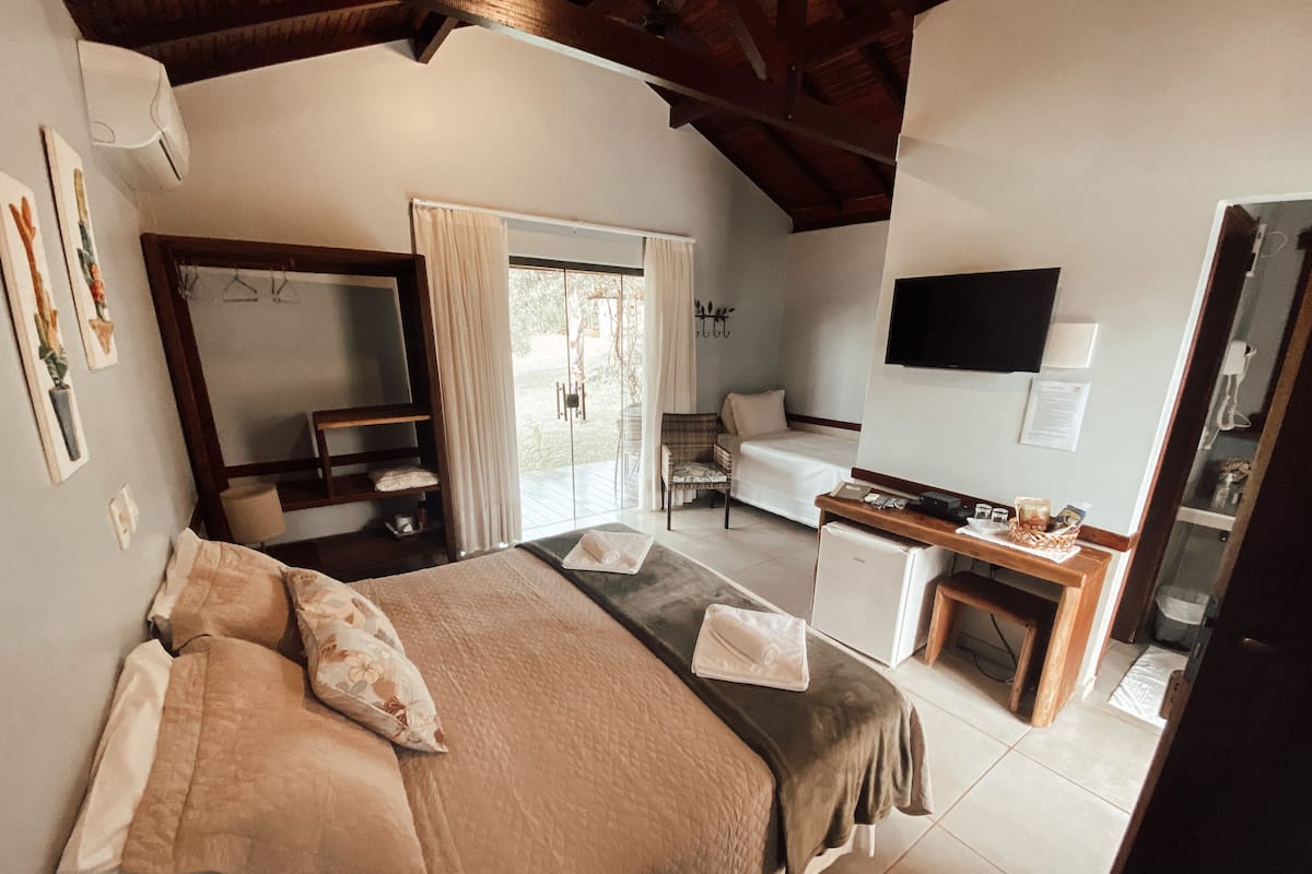 A bedroom with a bed, a desk, a chair, a TV, and a window.