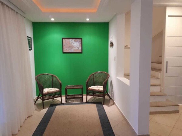 Un pasillo con paredes verdes, dos sillones de mimbre, una mesita y un mapa enmarcado en la pared.