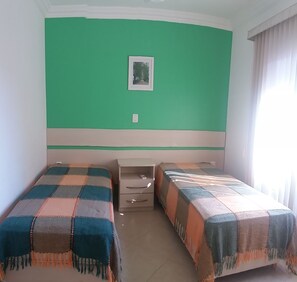 Una habitación con dos camas, un pequeño aparador, un cuadro en la pared y una ventana con cortinas.