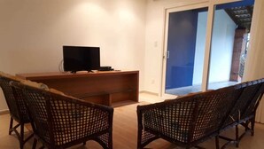 A room with a wooden desk, a television, and two wicker chairs.