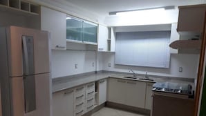 A compact kitchen with white cabinets, a stainless steel refrigerator, a sink, and a window with blinds.