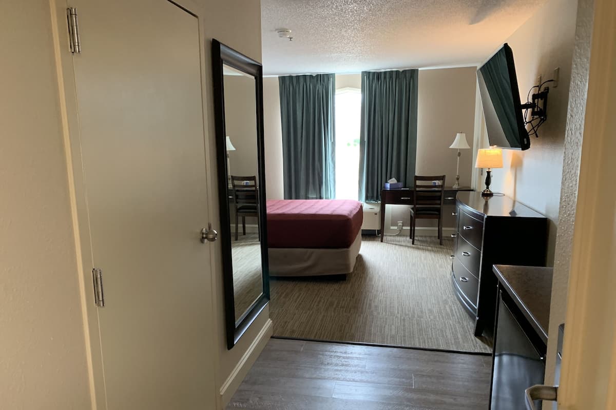Ein Hotelzimmer mit Bett, Schreibtisch, Stuhl, Kommode und Fernseher.