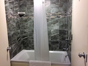 A bathroom with a bathtub, a shower curtain, and a tiled wall with a mosaic pattern.