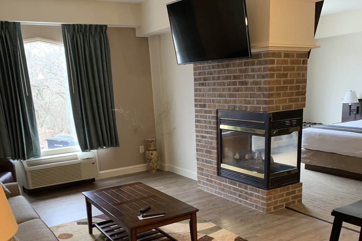 Ein Wohnzimmer mit Kamin, einem flachbildfernseher darüber, einem Sofa, einem Couchtisch und einem Bett mit Lampe.