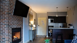 A living room with a brick fireplace, a blue sofa, a coffee table, and a kitchen area with a microwave and refrigerator. - McCoy's Inn (Ripley)