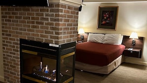 A hotel room with a brick fireplace, a bed with a red blanket, two bedside lamps, and a framed picture on the wall. - McCoy's Inn (Ripley)
