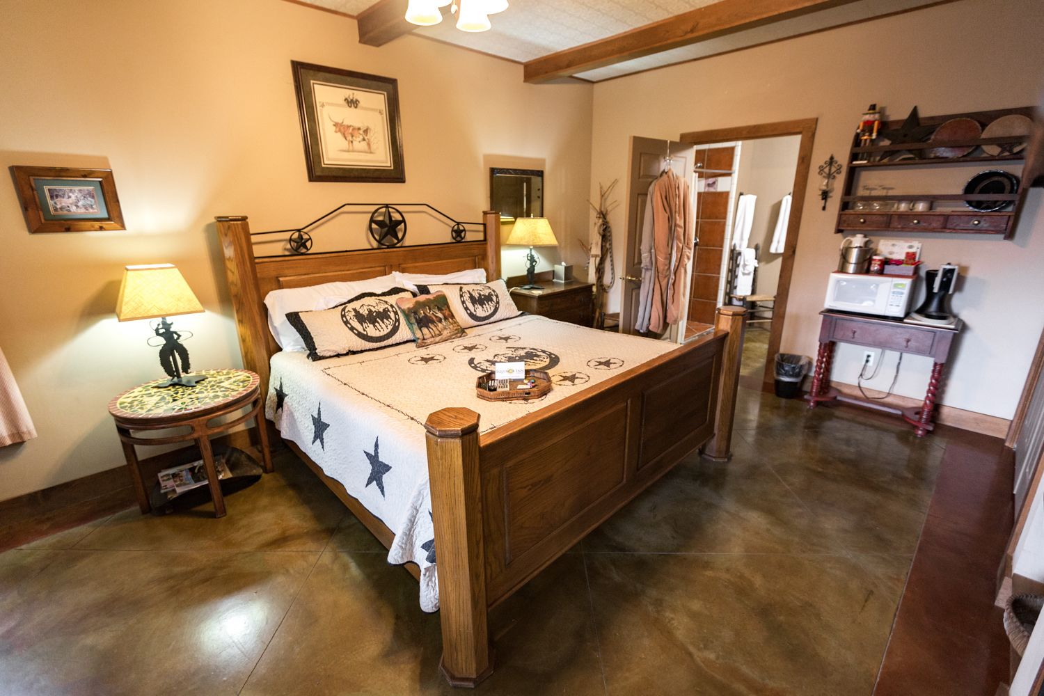 A traditional wooden bed with a star-patterned bedspread, two bedside tables with lamps, a wooden nightstand, and a small round table with a lamp.