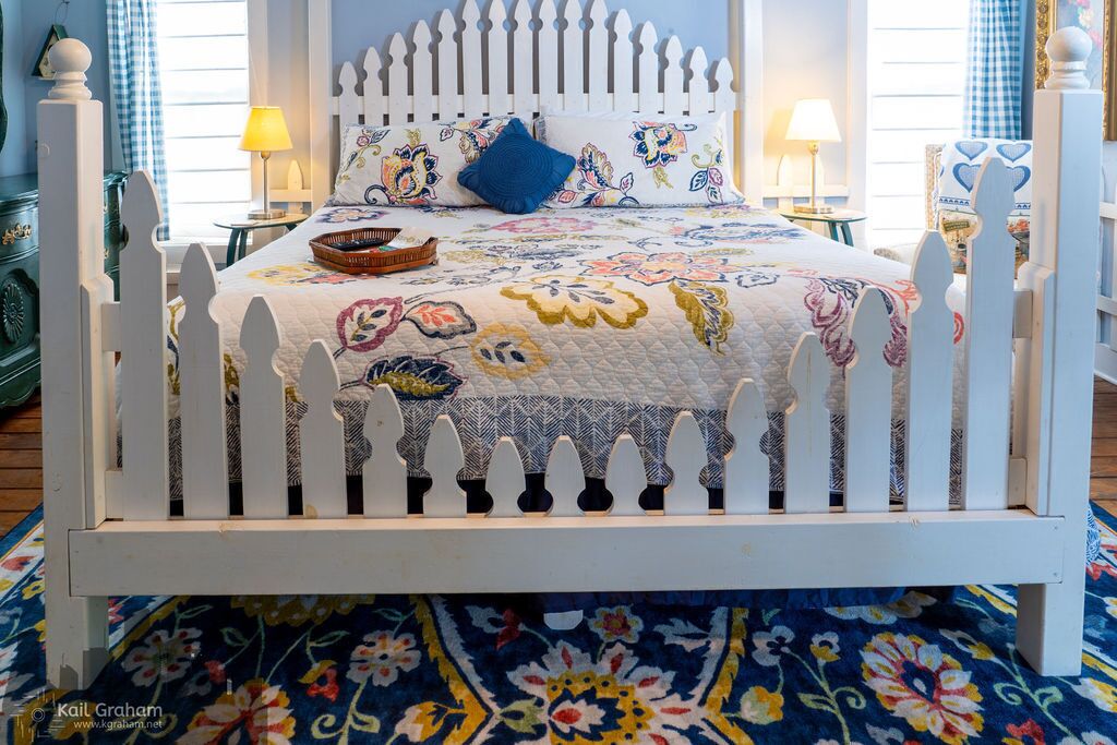 A bed with a white picket fence, a floral-patterned bedspread, and a blue pillow.