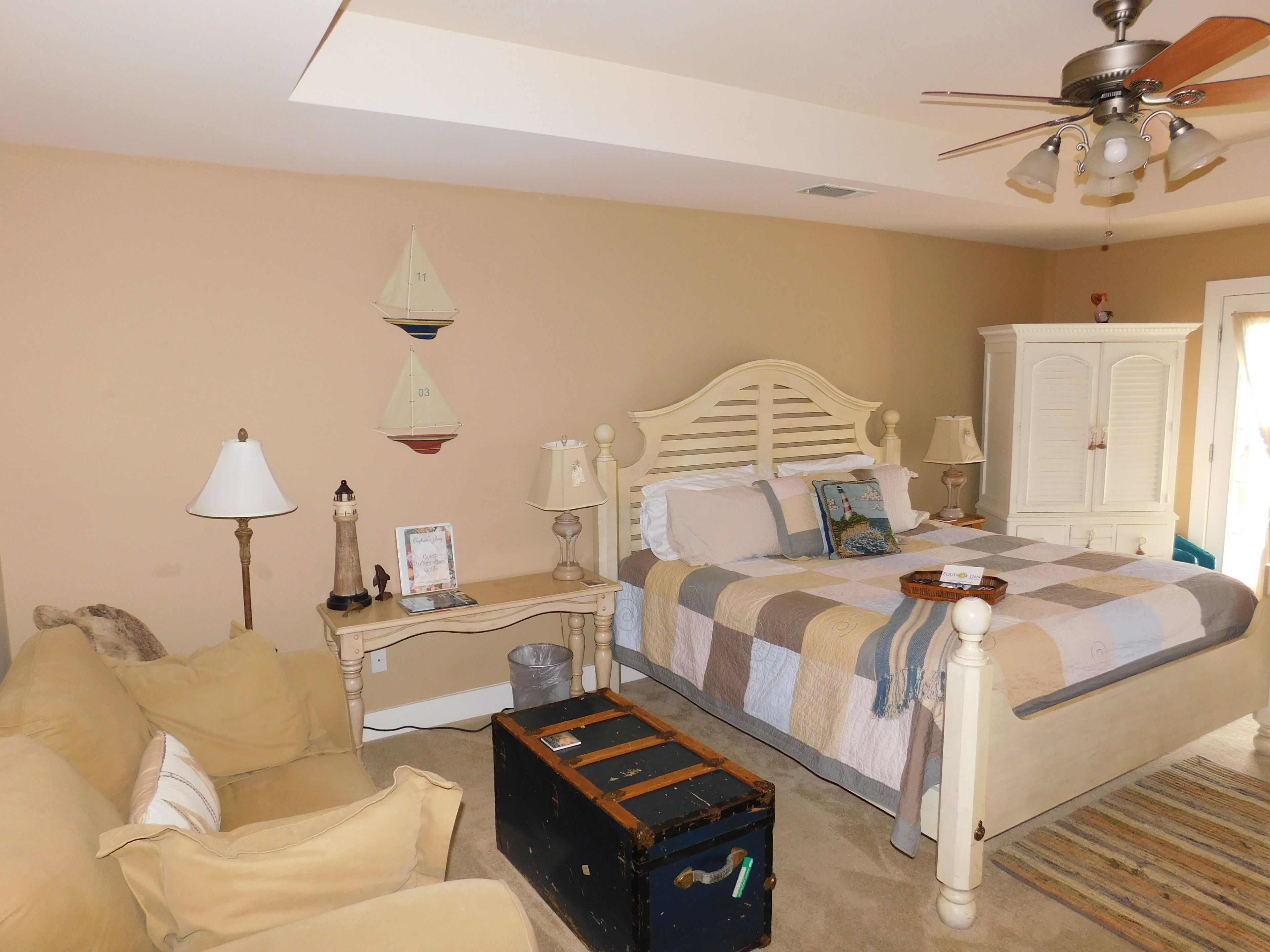 A bedroom with a bed, a nightstand, a lamp, a chest of drawers, a suitcase, and a ceiling fan.