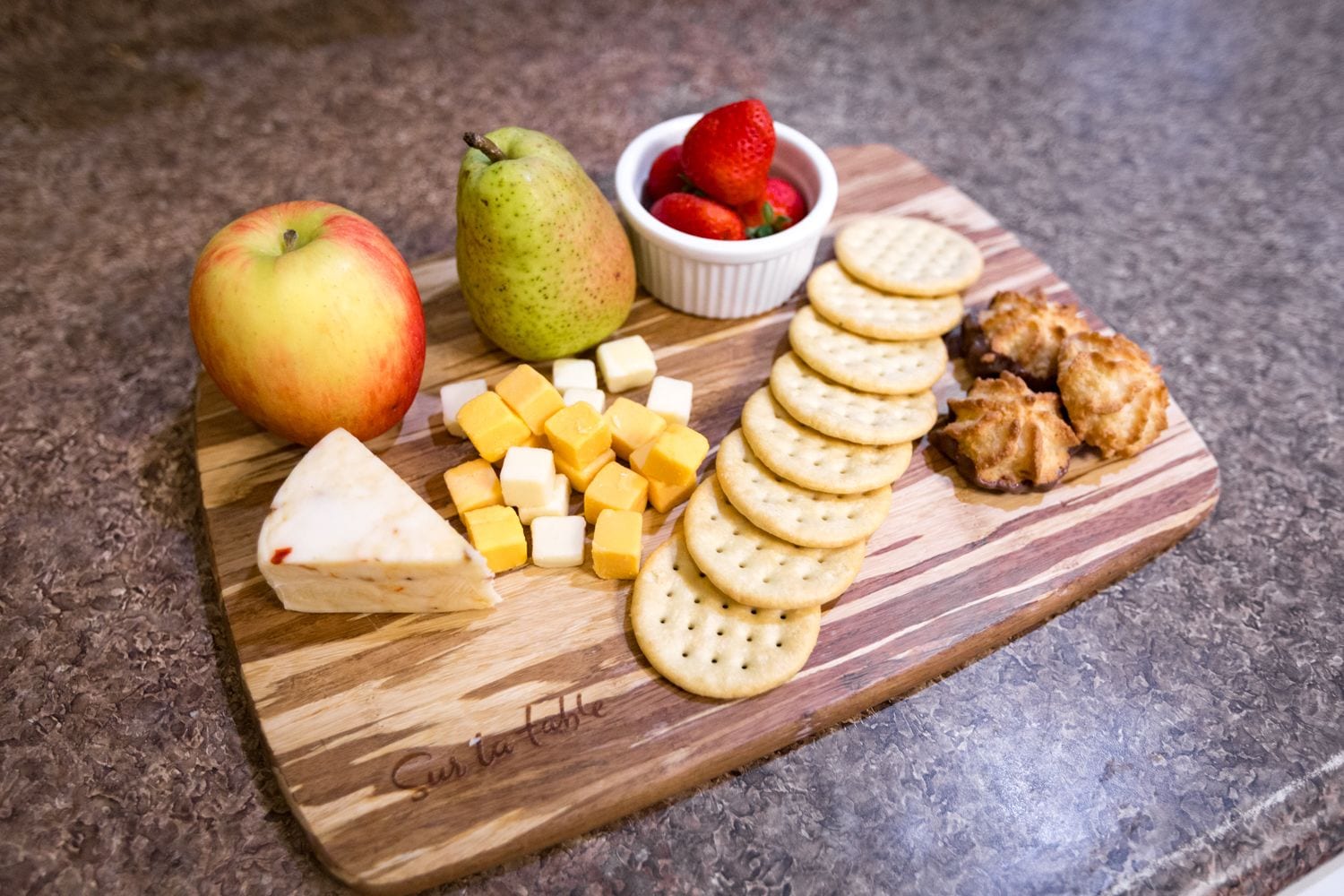 Una tabla de madera con diversos alimentos, como queso, galletas y frutas.