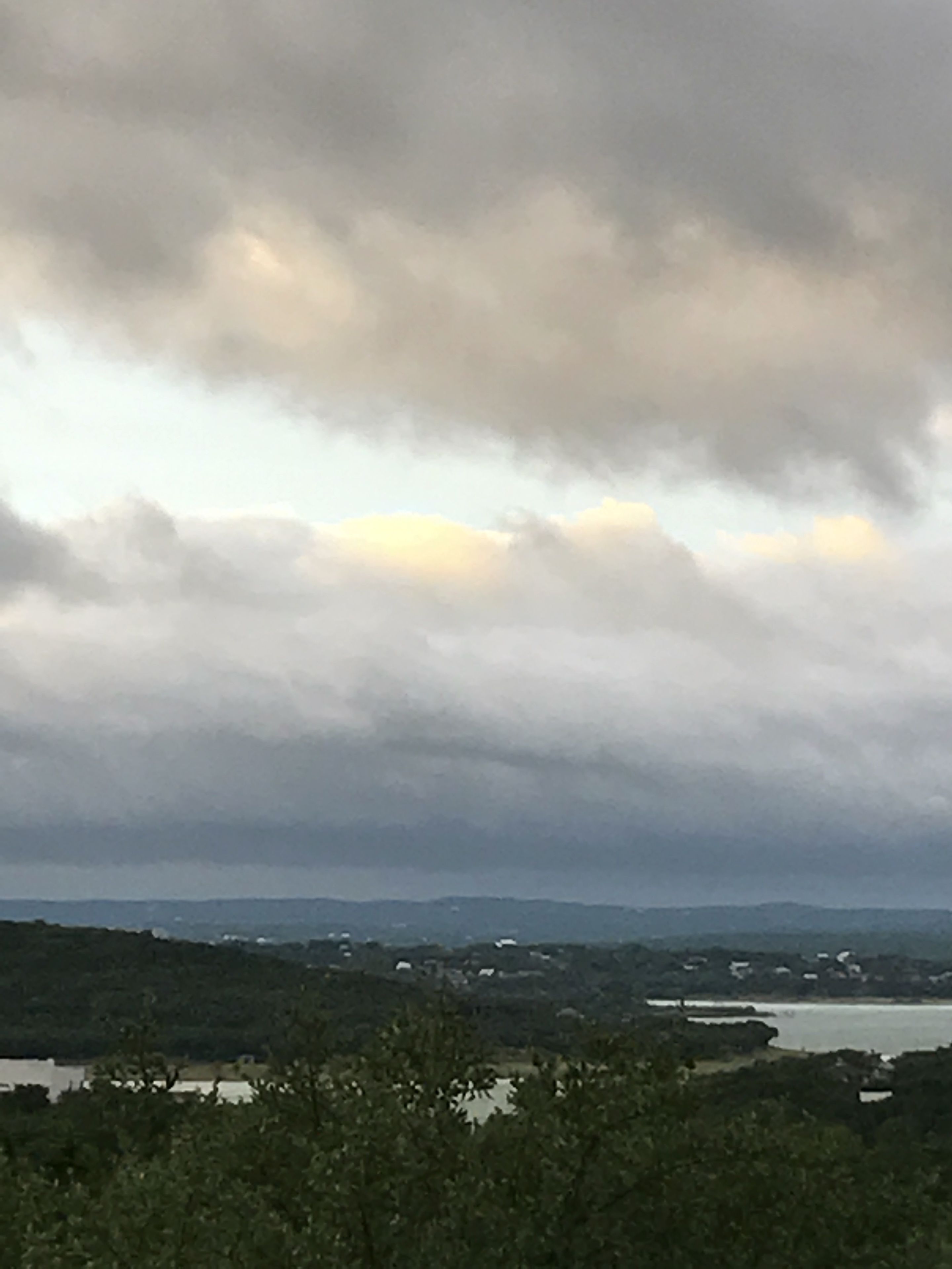 A coastal landscape with a body of water, hills, and a cloudy sky.