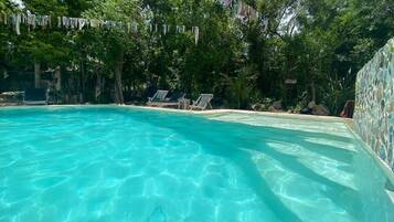 A clear blue pool surrounded by lounge chairs and trees.