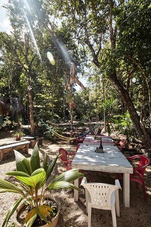 An outdoor patio with a wooden table and chairs, surrounded by greenery and trees. - Corazón de Selva (Macario Gomez)