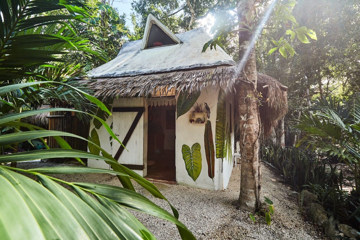 A small, rustic hut with a thatched roof, surrounded by lush greenery.