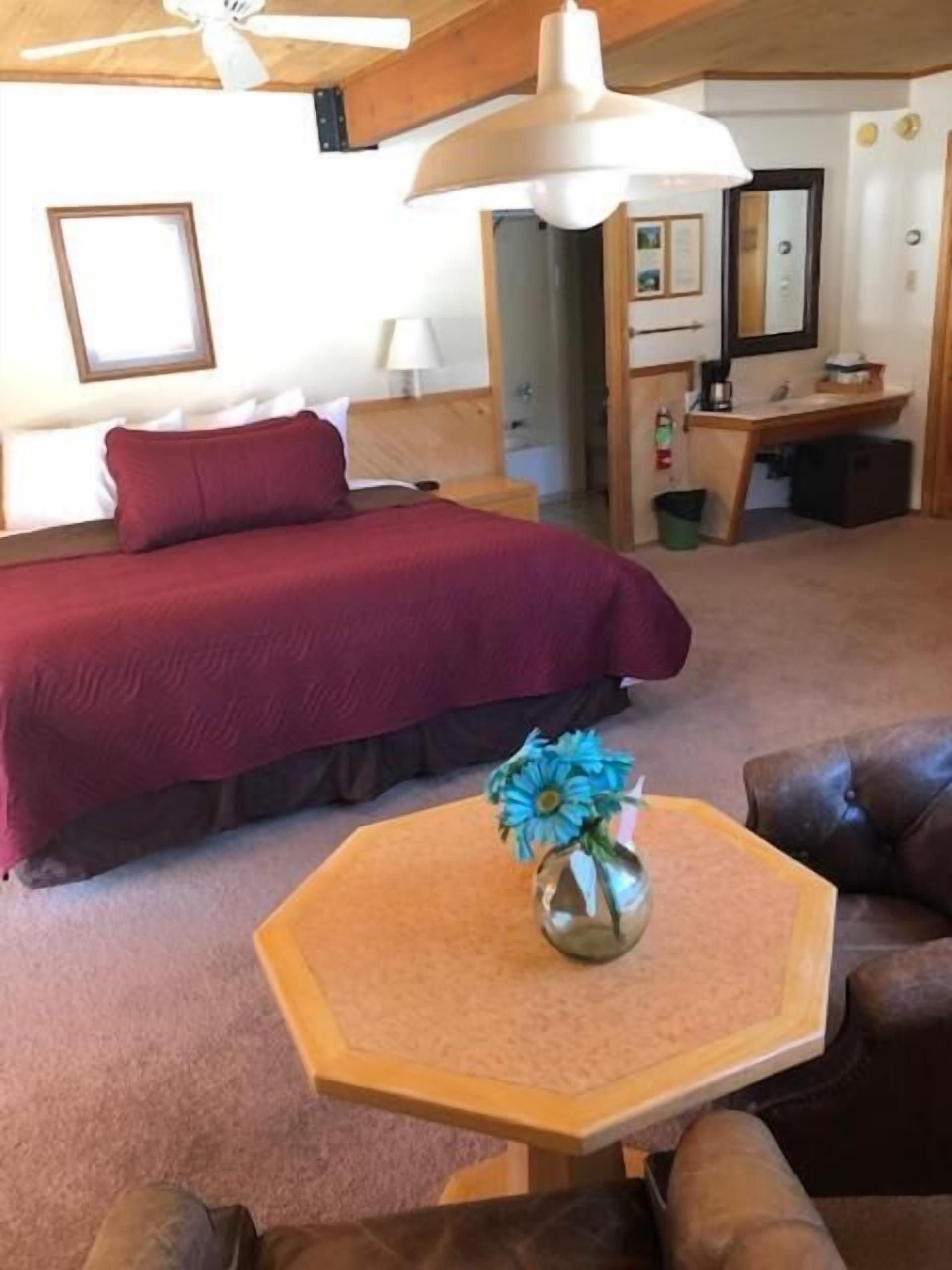 Een slaapkamer met een groot bed, een bureau en een stoel. Op een bijzettafeltje staat een vaas met bloemen.