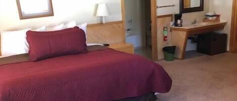 Een slaapkamer met een groot bed, een bureau en een stoel. Op een bijzettafeltje staat een vaas met bloemen.