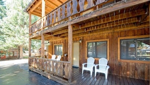 Una cabaña de madera con balcón, dos sillas blancas y una terraza de madera.