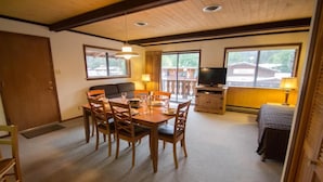 Un comedor con una mesa y sillas de madera, un sofá, un televisor y un balcón con vistas.