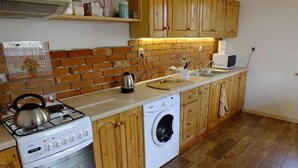 Una cucina compatta con piano cottura a gas, lavatrice, mobili in legno e zoccolo di mattoni.