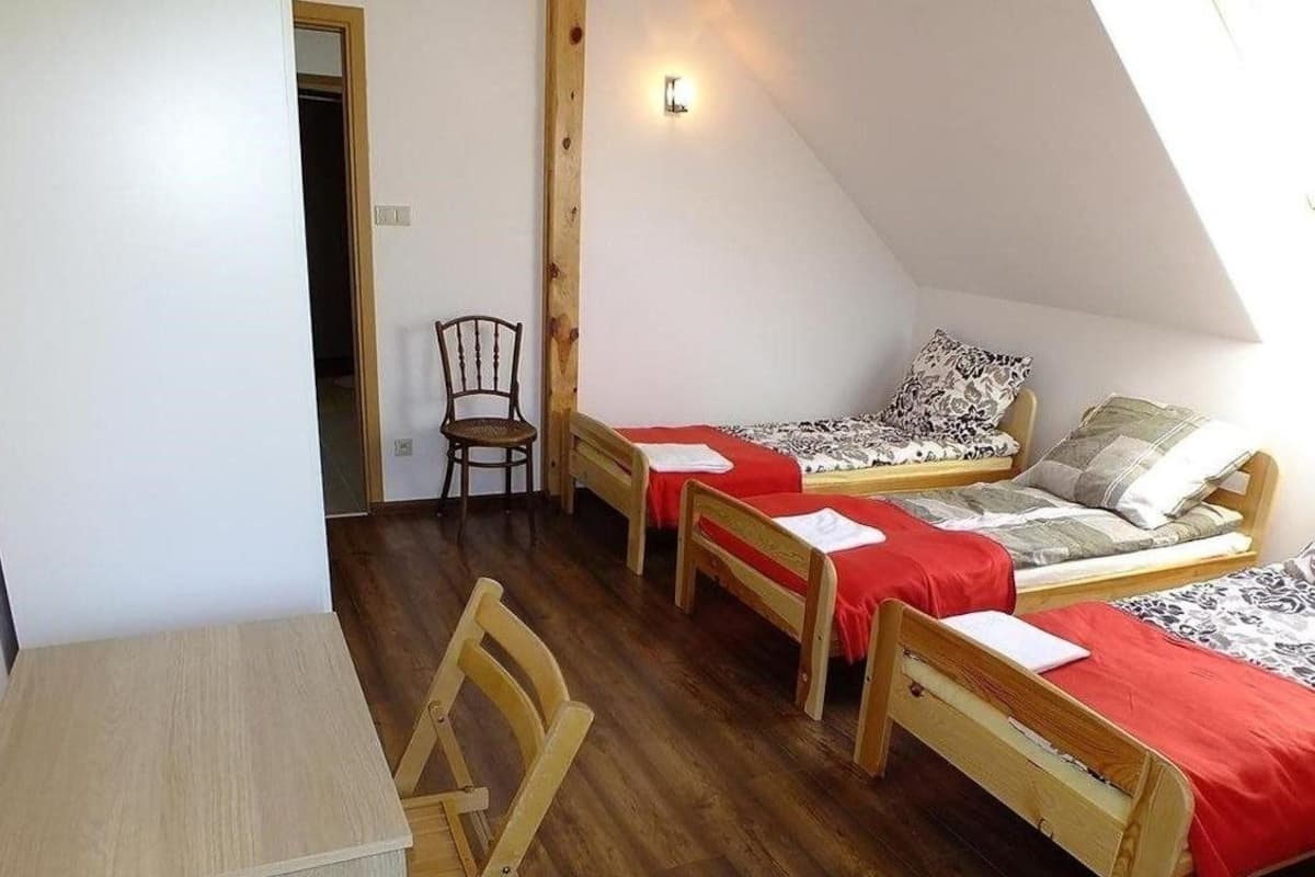 Une chambre de dortoir avec trois lits en bois, un bureau en bois et une chaise.