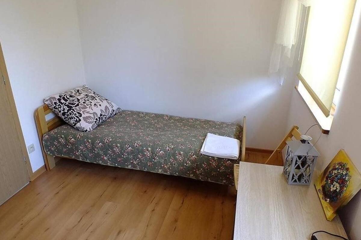 Une petite pièce avec un lit simple, une table en bois, une lampe et un tableau.