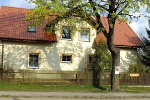 A two-story building with a red-tiled roof, a wooden fence, and a tree in front. - Agroturystyka Wielkie Leźno (Brzozie)