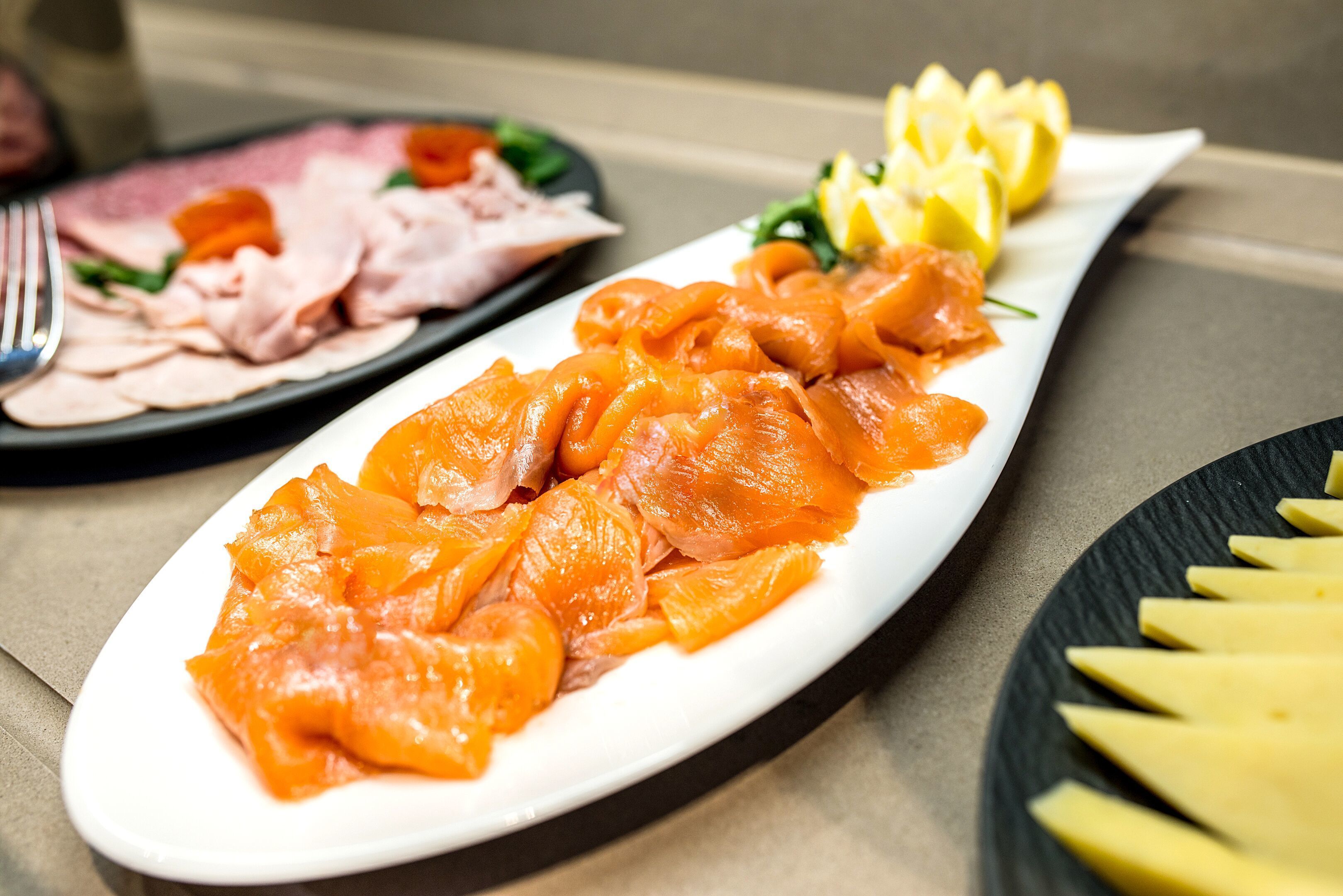 A plate of smoked salmon with lemon slices and a side of sliced cheese.