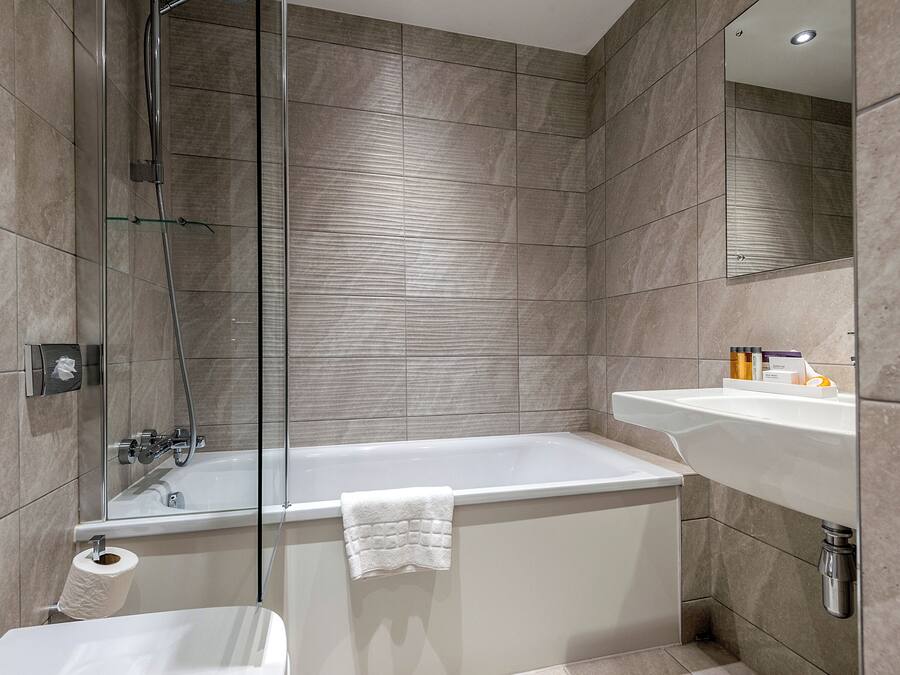 A modern bathroom with a glass-enclosed shower, a white bathtub, and a sink with toiletries.