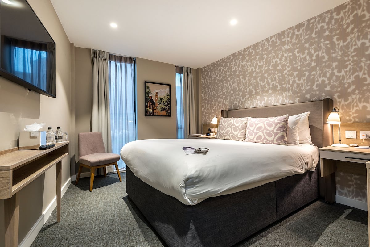 Una habitación de hotel moderna con una cama grande, un escritorio, una silla y un televisor.