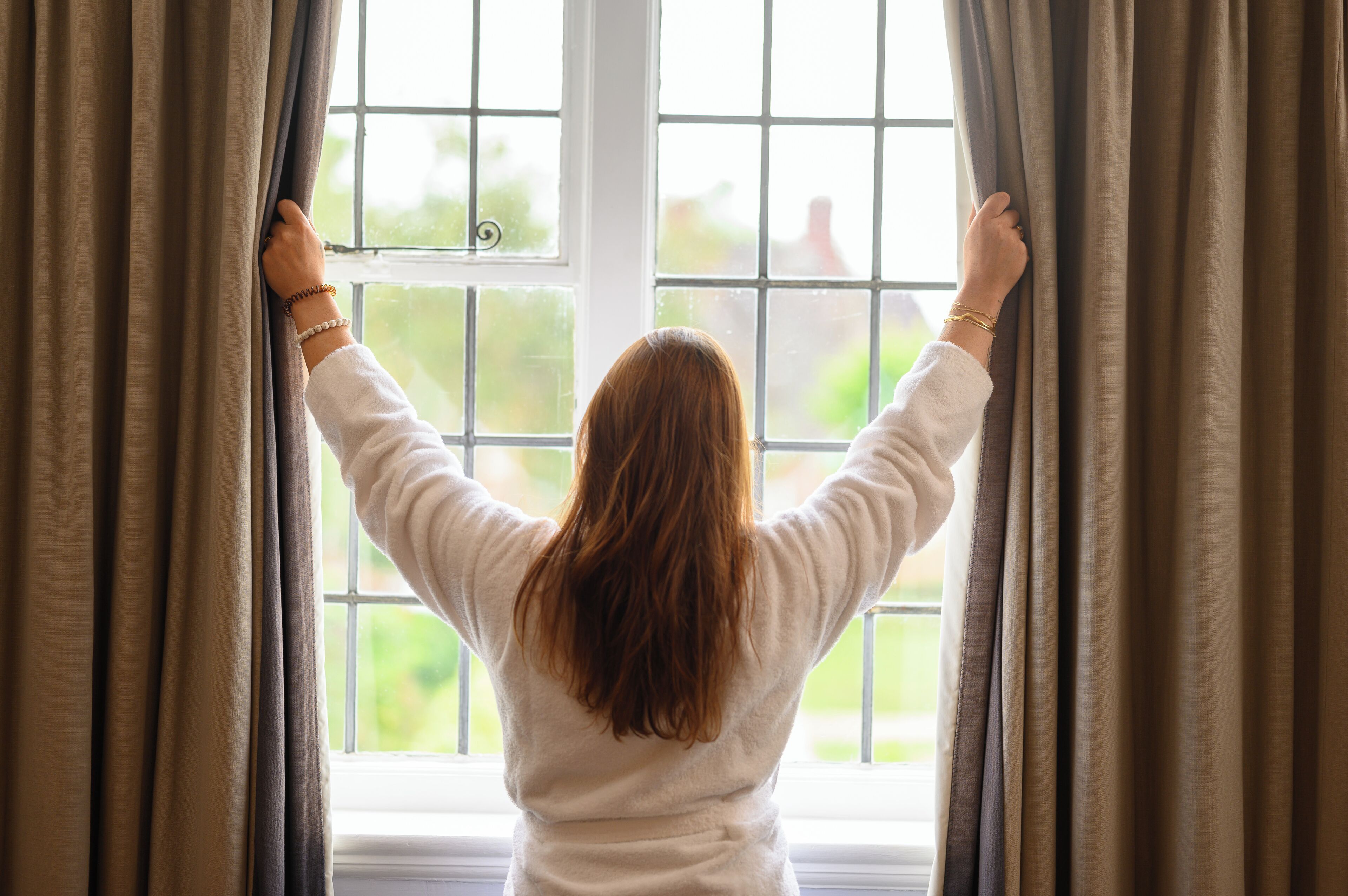 A person standing by a window with curtains, looking outside.