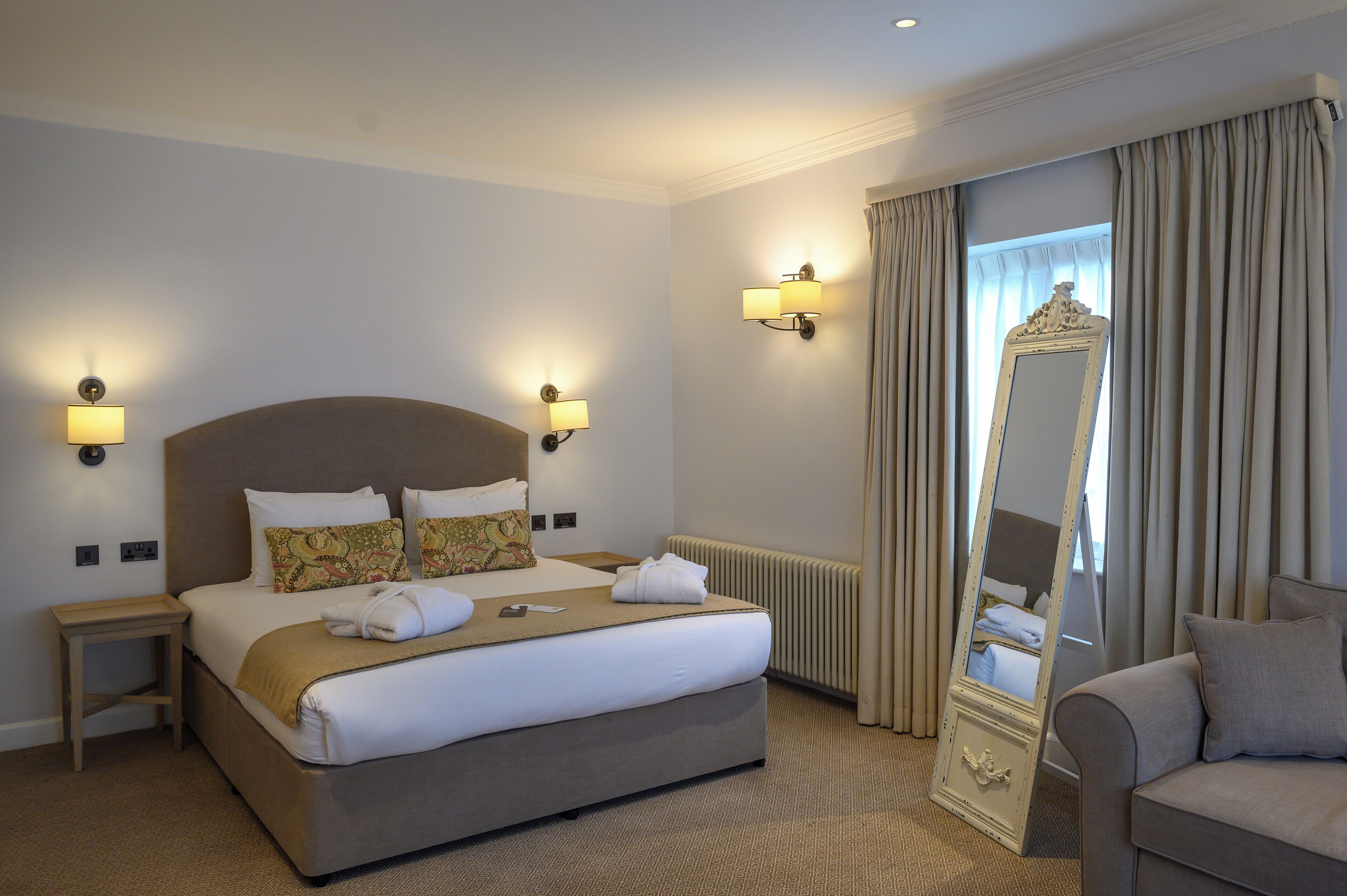 A hotel room with a large bed, bedside lamps, a mirror, a sofa, and a radiator.