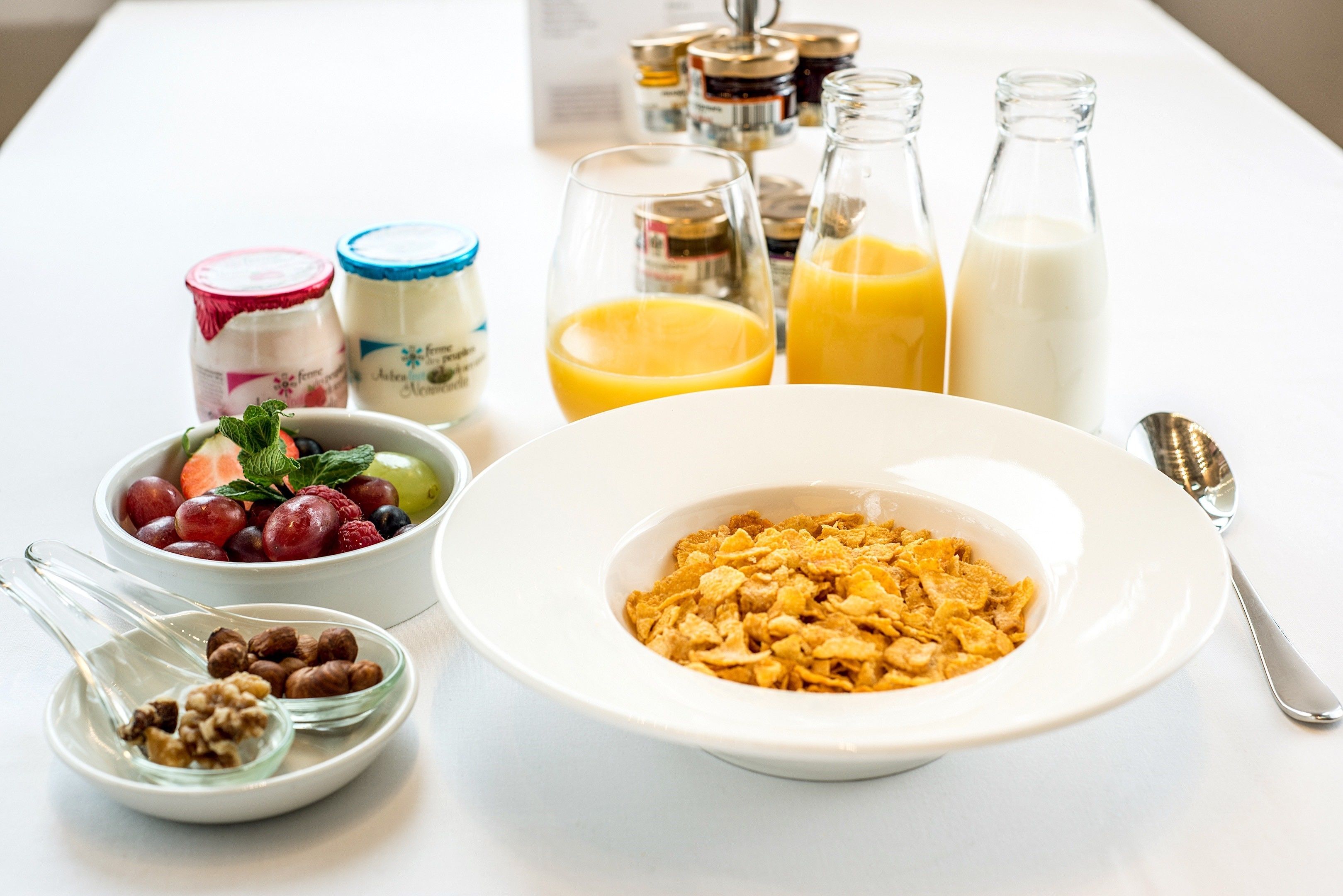 A breakfast setting with cereal, yogurt, fruit, and milk.