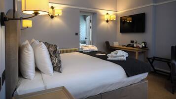 A hotel room with a large bed, bedside lamps, a desk with a chair, a TV, and a view of the hallway.